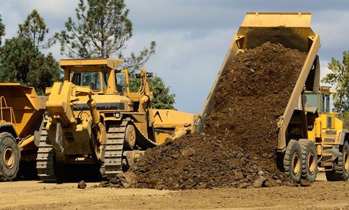 Dumptruck unloading near a roadway for preparation.